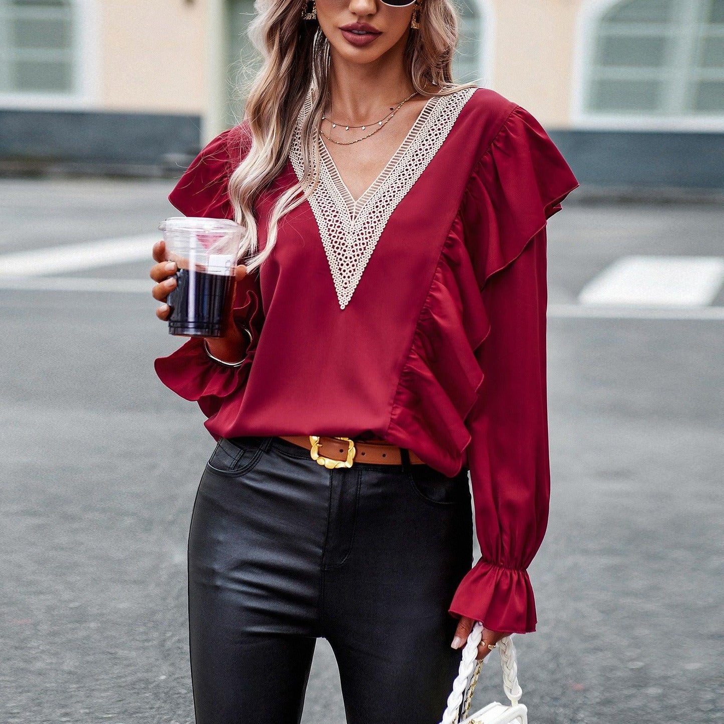 Woman wearing Demure Commuter V-Neck Long Sleeve Shirt in burgundy with lace details, holding a coffee, stylish urban setting