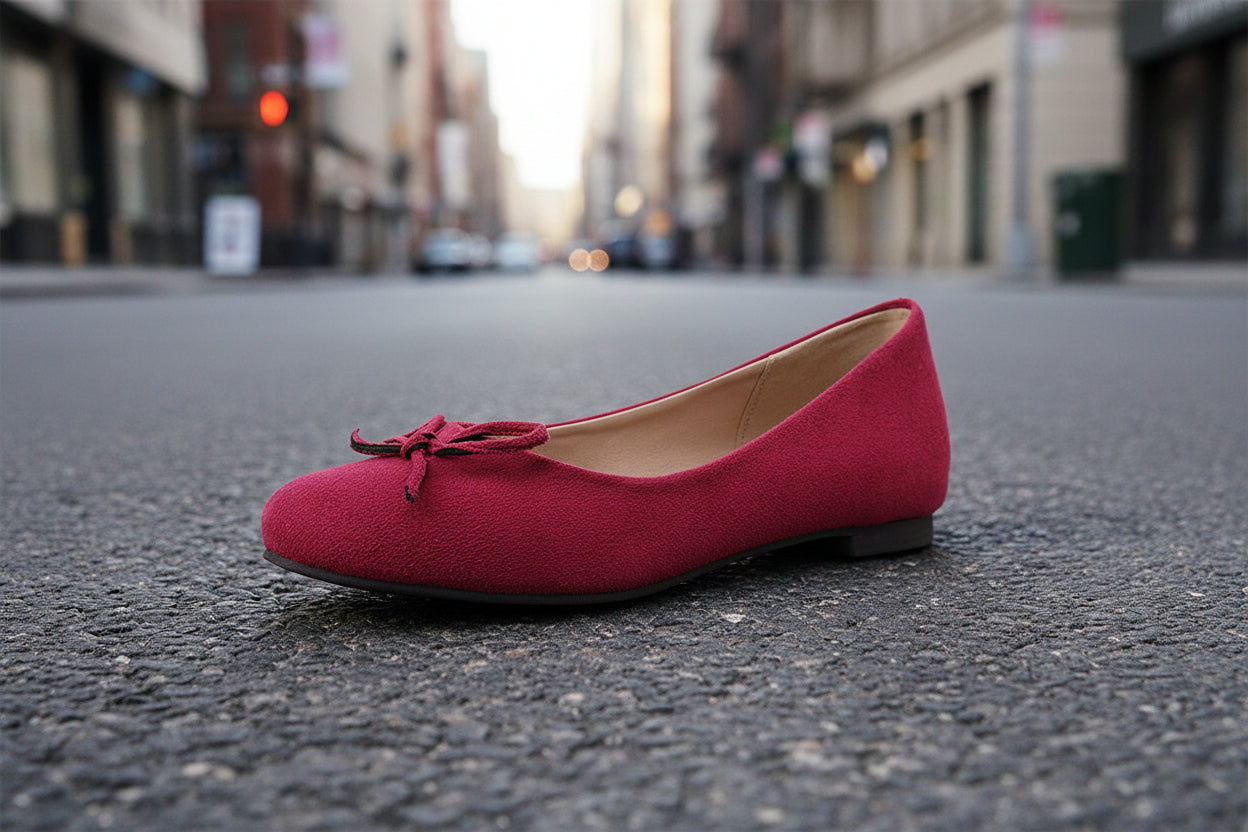 Red ballet flat shoe with bow, sitting on urban street pavement