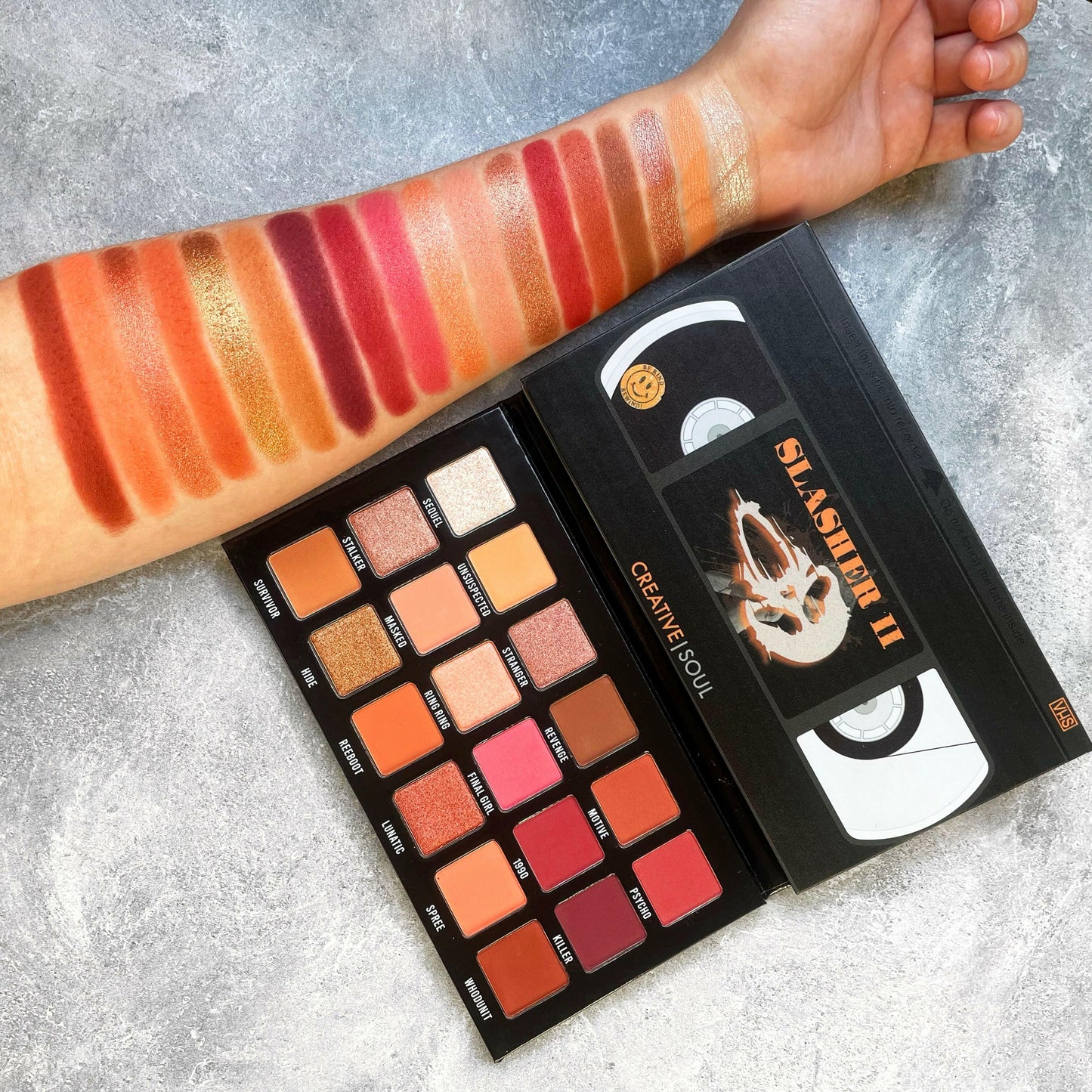 Slasher II Eyeshadow Palette with neutral shades inspired by 90s VHS horror films, shown on a forearm for color swatch display.