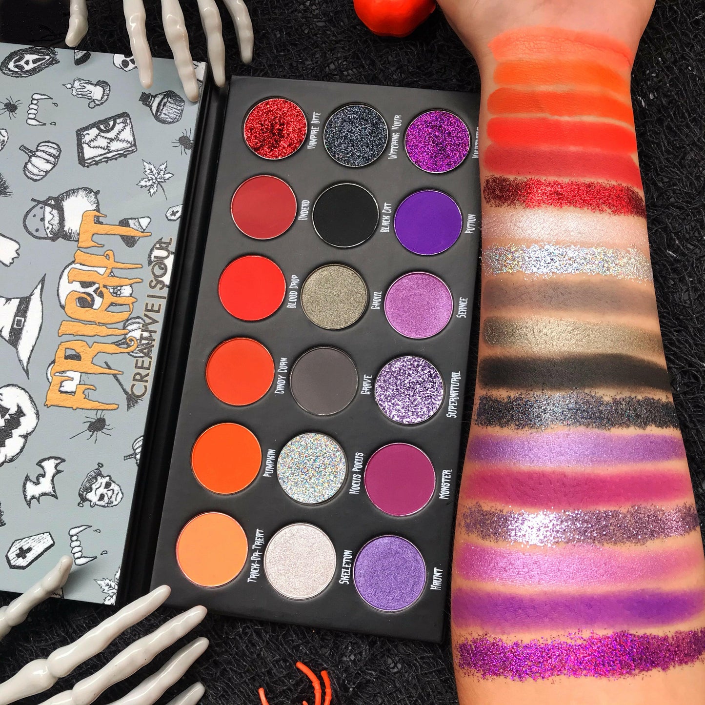 FRIGHT Eyeshadow Palette with vibrant Halloween shades of purples, reds, oranges, grays; includes swatch samples on arm.