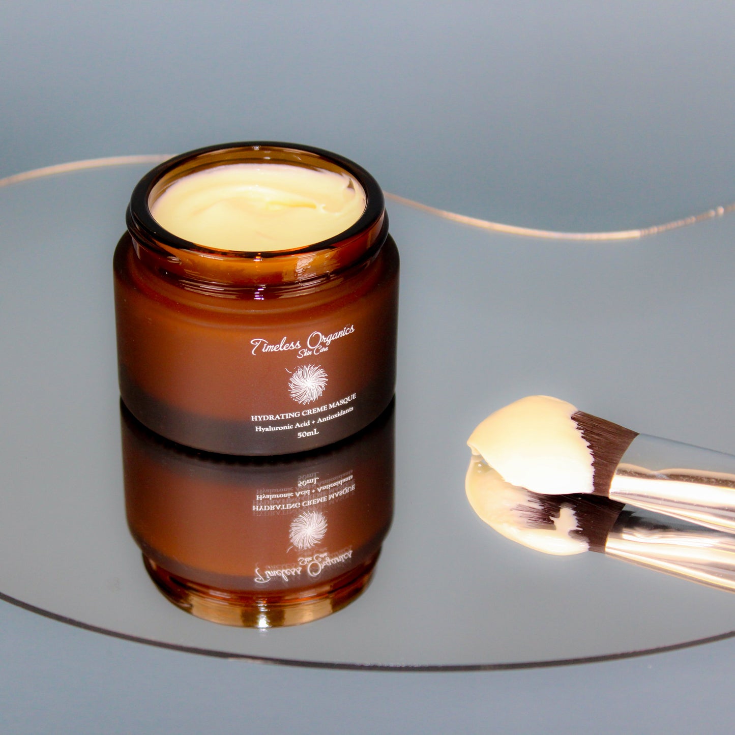 Deep Hydration + Antioxidant Creme Masque in amber jar with application brush, offers soothing, hydrating, and antioxidant benefits.