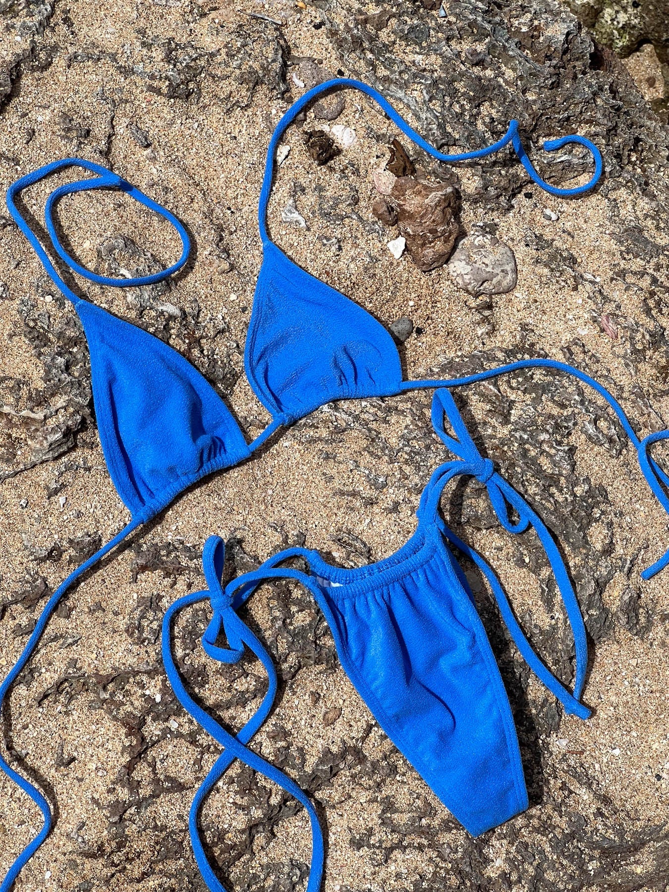 olivia bottom - valencia bikini set in blue terry fabric with adjustable ties on sandy rocks
