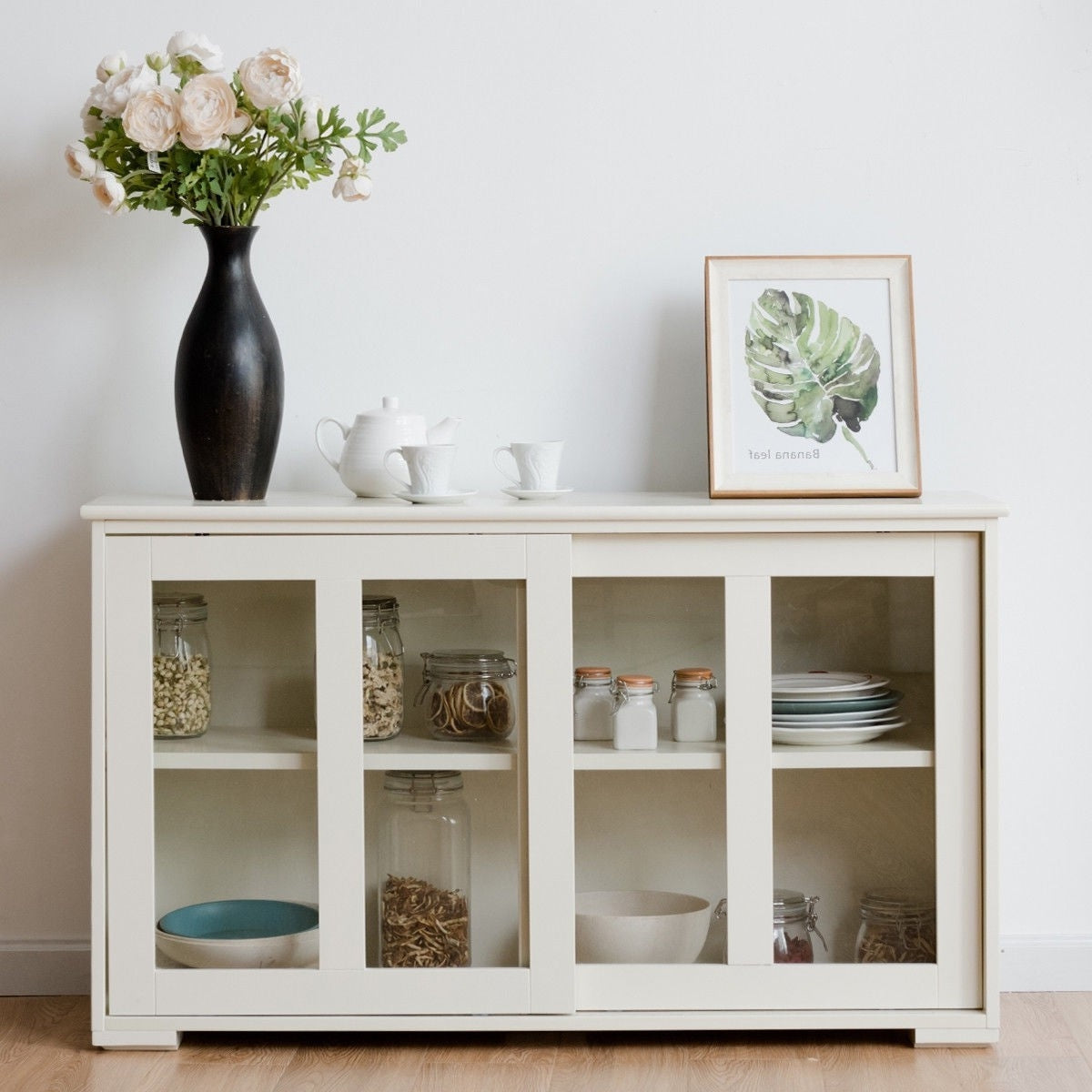 Modern White Wood Buffet Sideboard Cabinet with Glass Sliding Door in a dining room setting with decor items on top.