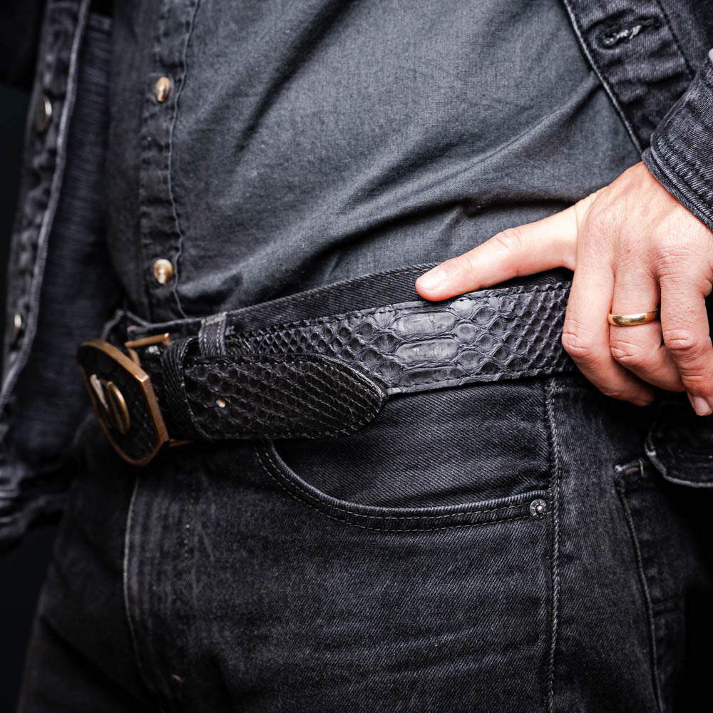 Arkansas Belt Black in genuine python skin with antique brass buckle displayed on a person wearing dark denim.