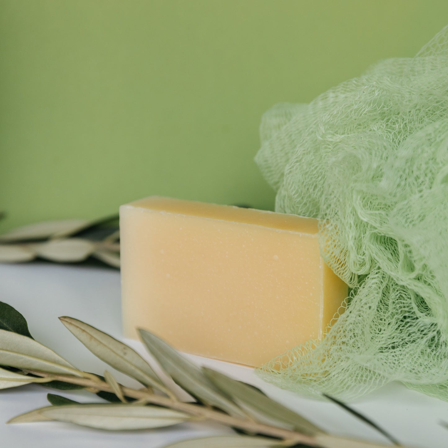 White Tea + Ginger Shave Bar with lush lather and soothing skincare benefits, surrounded by green netting and leaves, on a green background.