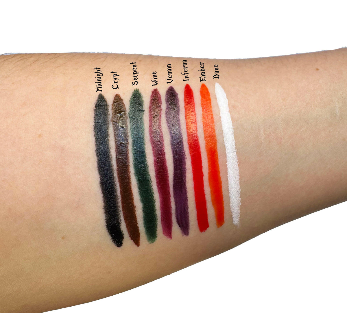 Swatches of liquid eyeliner shades on skin, featuring Midnight, Crypt, Serpent, Wine, Volcano, Inferno, Ember, and Dove.