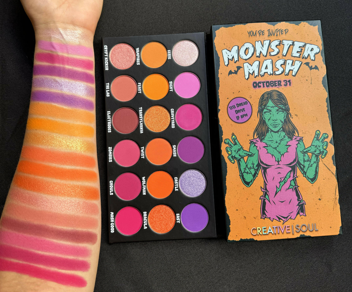 Monster Mash Eyeshadow Palette with 18 vibrant pink, orange, purple shades next to swatches on arm, perfect for Halloween makeup.
