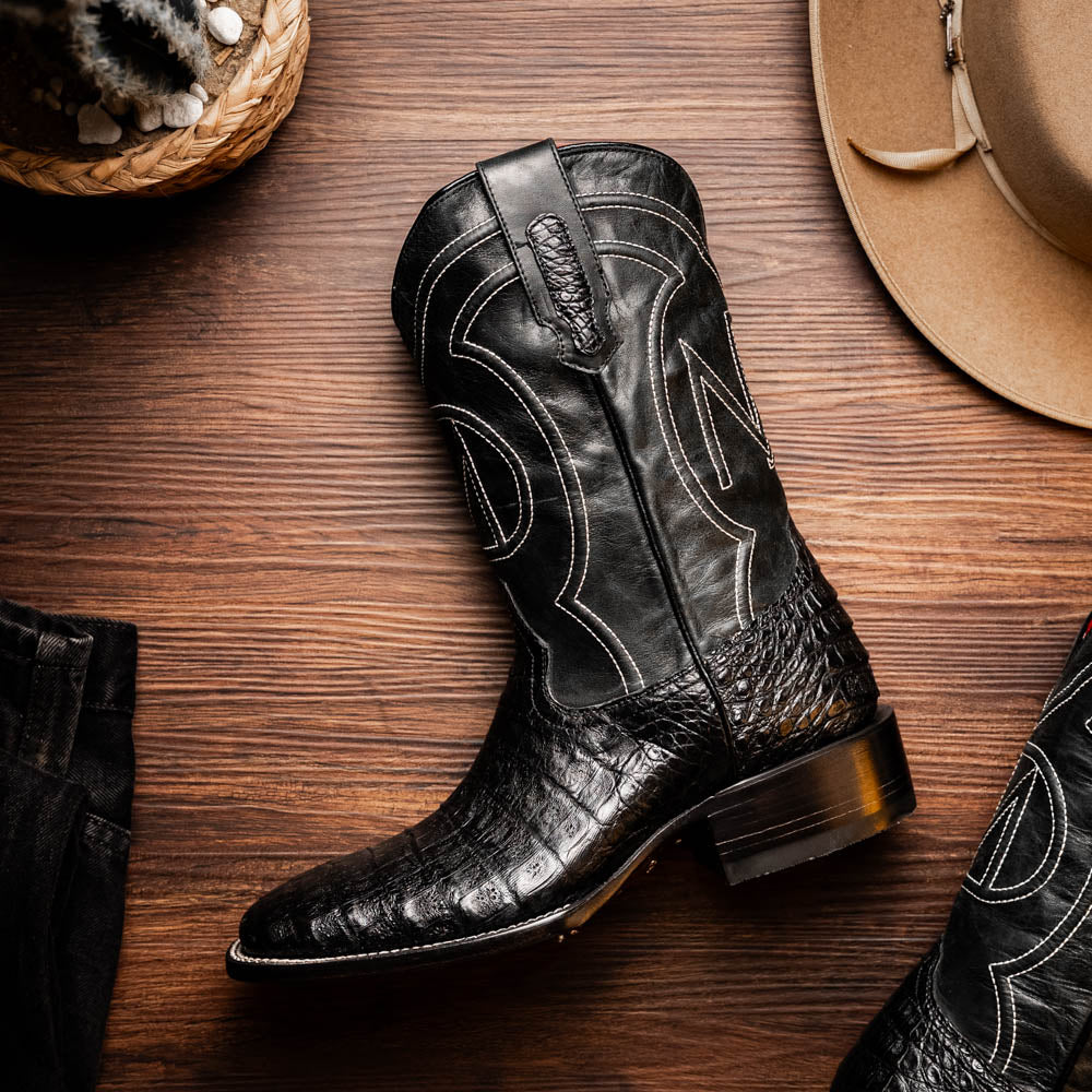 Tucson Black caiman belly skin cowboy boot on wooden surface, showcasing Western craftsmanship and square-toe design.
