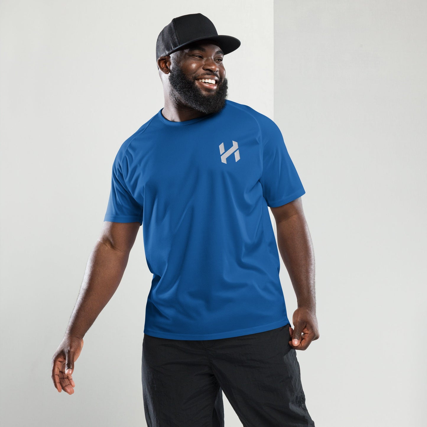 Man wearing a blue athletic shirt and black cap, smiling confidently.