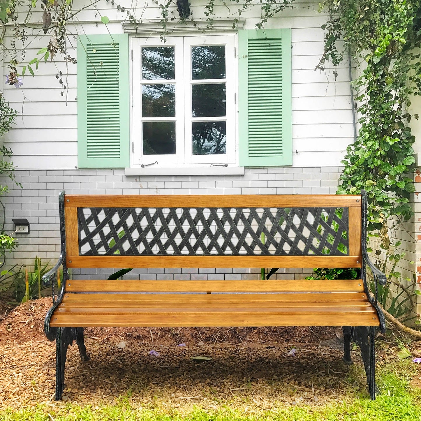 Outdoor Cast Iron Patio Bench with wooden seat and decorative PVC backrest, ideal for garden seating against a white house backdrop.