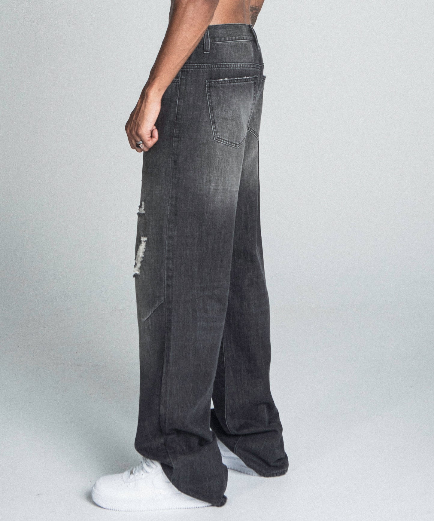 Model wearing AJ09B-2 BLACK DISTRESSED BAGGY JEANS with faded details, mid-rise waist, and loose-fit silhouette, showing back pocket design.