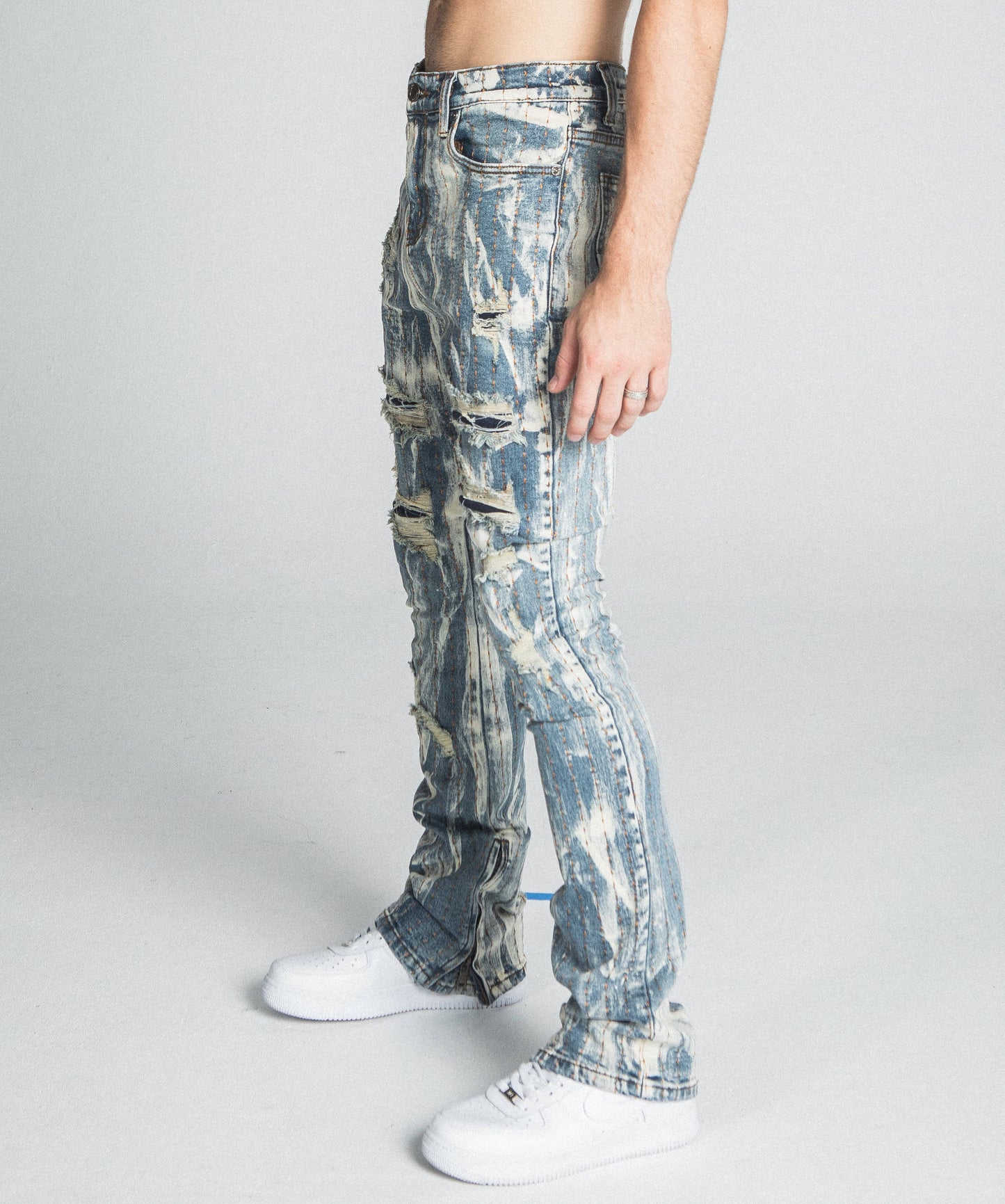 Man wearing AJ17SK THREAD LINE STACKED JEANS with vintage wash and mid-rise waist, showing side profile in minimalist setting.