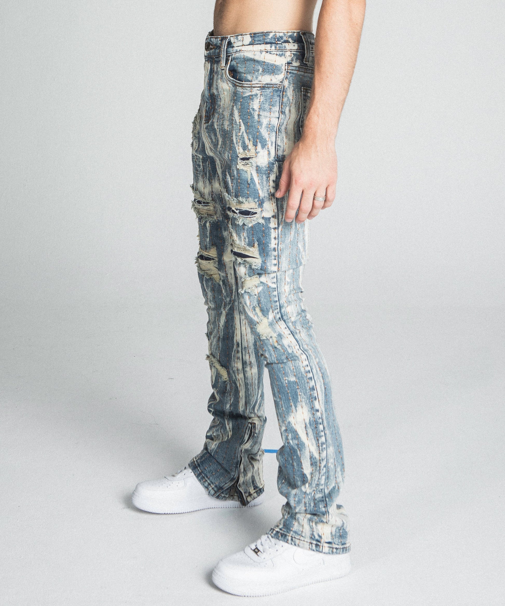 Man wearing AJ17SK THREAD LINE STACKED JEANS with vintage wash and mid-rise waist, showing side profile in minimalist setting.