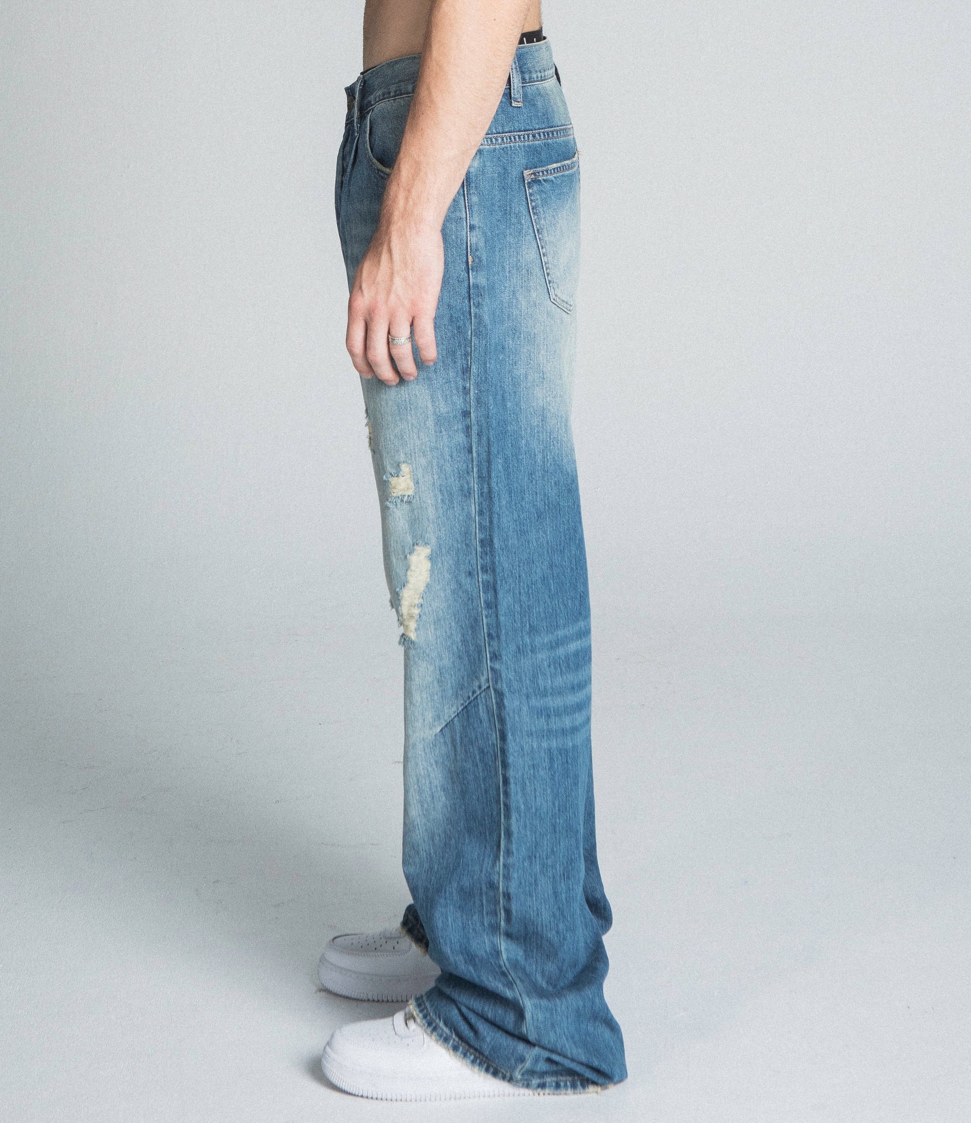 Side view of model wearing AJ09-3 CLASSIC BLUE LIGHTLY DISTRESSED BAGGY JEANS with mid-rise fit and faded details.