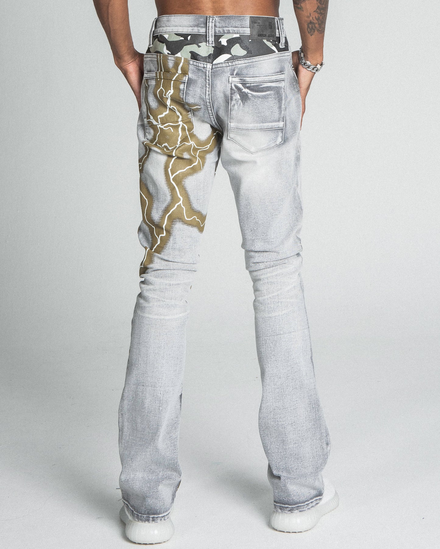 Rear view of AJ24SK LIGHTNING STACKED JEANS with gold lightning design on light denim, showcasing mid-rise waist and stacked legs.