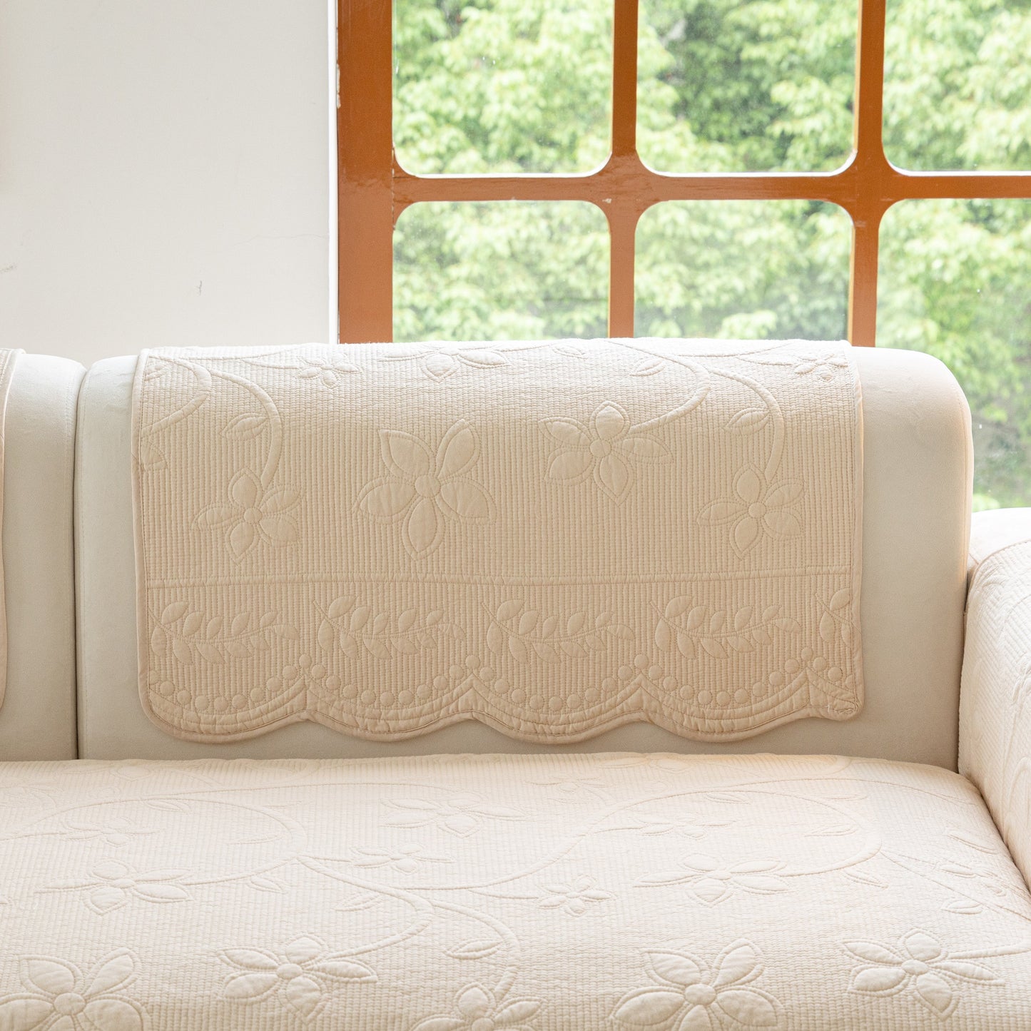 Floral Cotton Quilted Sofa Cover, Non-Slip Couch Protector with Scalloped Edges on a white sofa in front of a window.