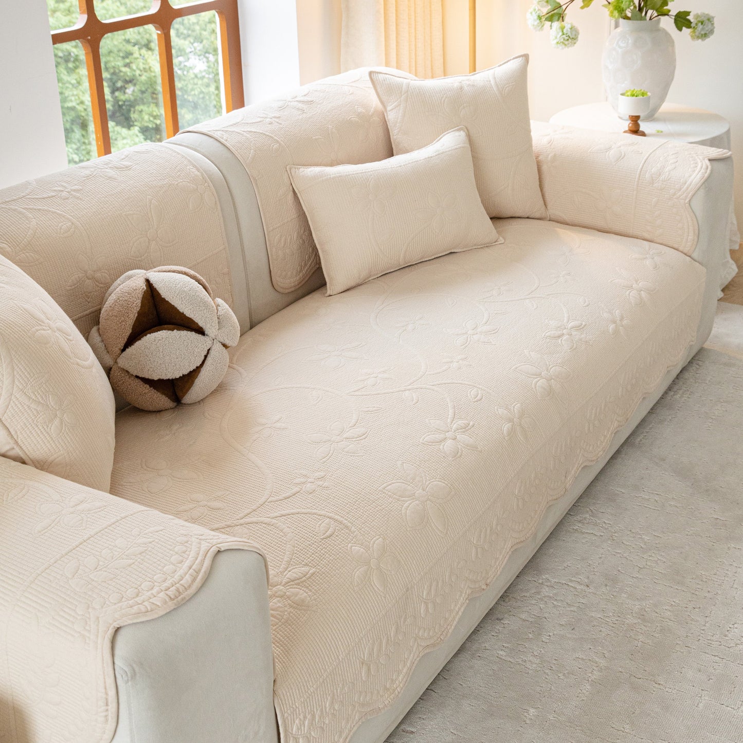 Floral Cotton Quilted Sofa Cover, Non-Slip Couch Protector with Scalloped Edges on beige sofa with cushions.