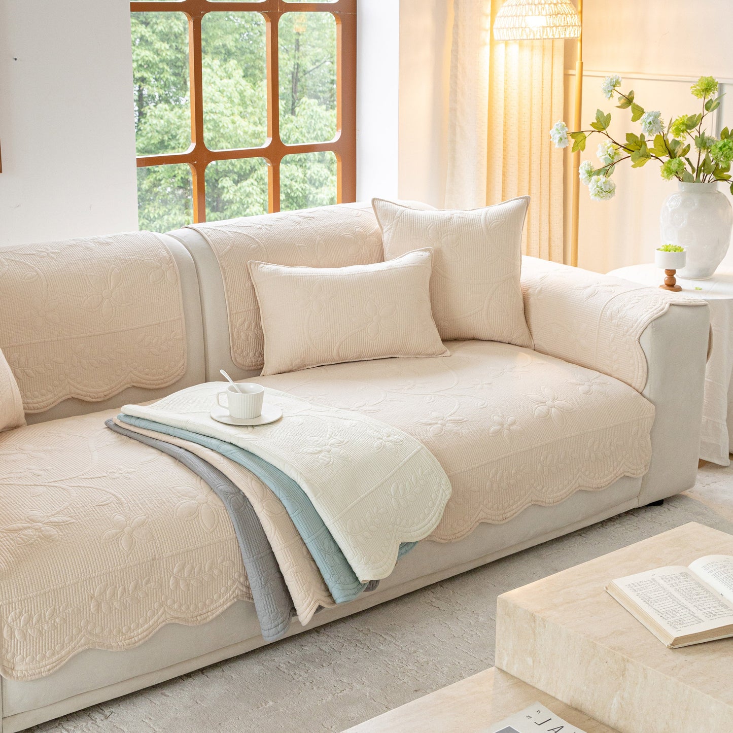 Floral Cotton Quilted Sofa Cover, Non-Slip Couch Protector with Scalloped Edges displayed on a beige sofa with pillows in a cozy living room.