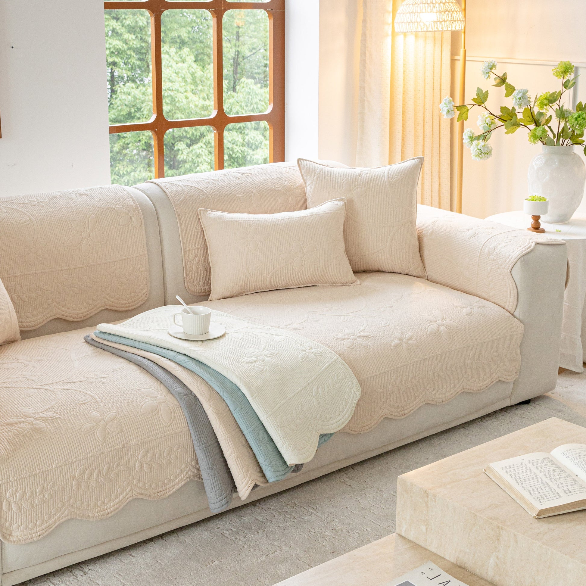 Floral Cotton Quilted Sofa Cover, Non-Slip Couch Protector with Scalloped Edges displayed on a beige sofa with pillows in a cozy living room.