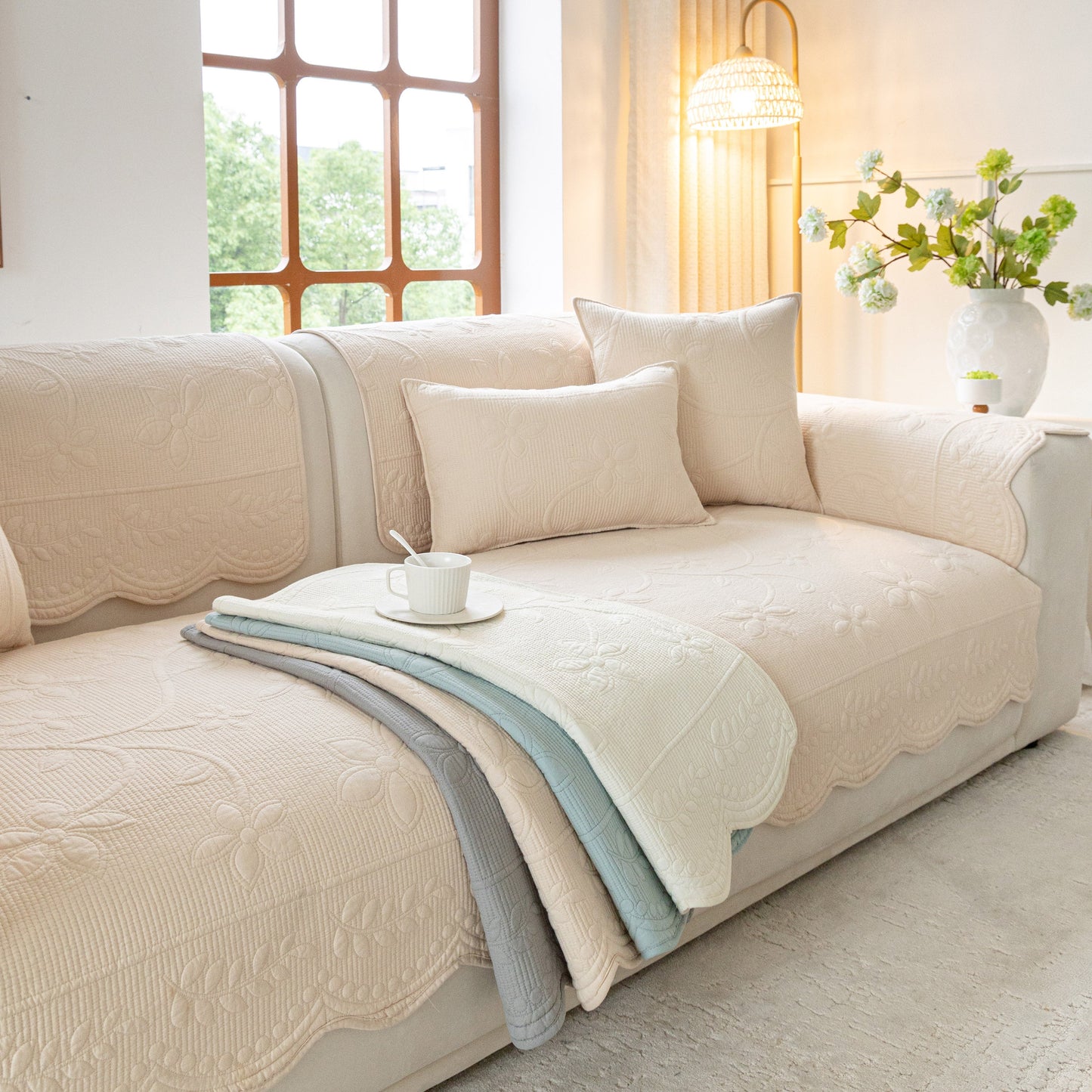 Floral Cotton Quilted Sofa Cover, Non-Slip Couch Protector with Scalloped Edges in a cozy living room setting with pillows.