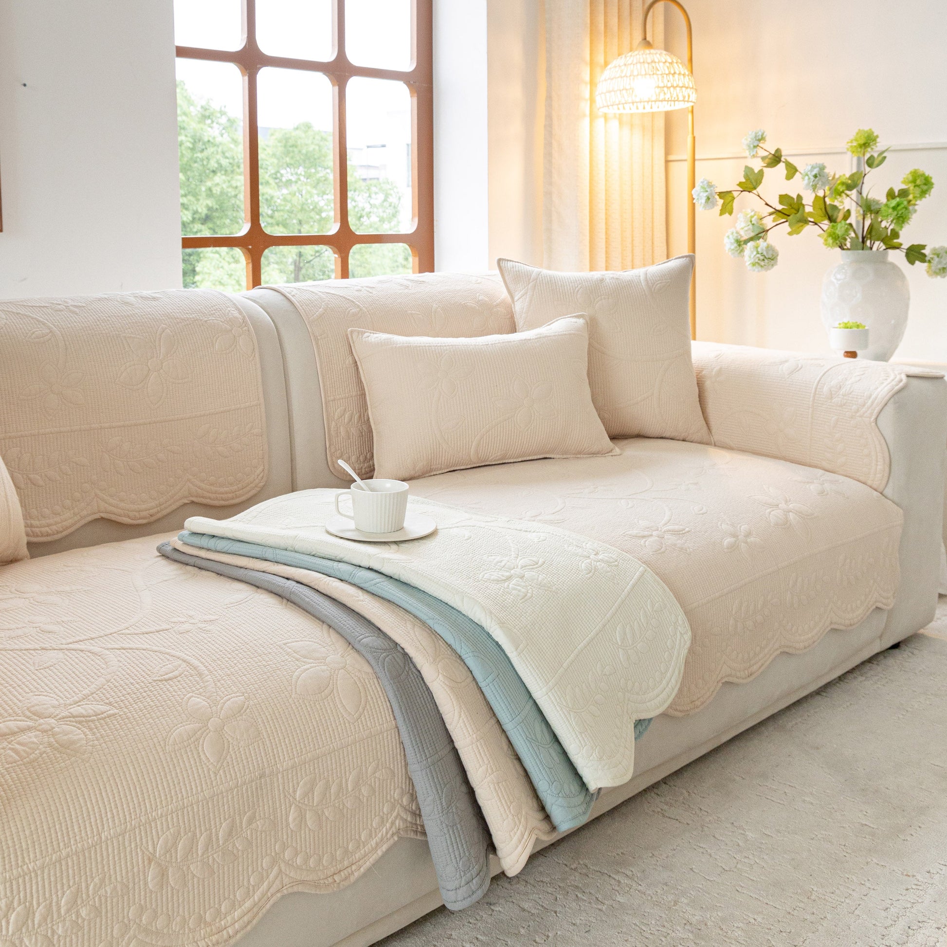 Floral Cotton Quilted Sofa Cover, Non-Slip Couch Protector with Scalloped Edges in a cozy living room setting with pillows.