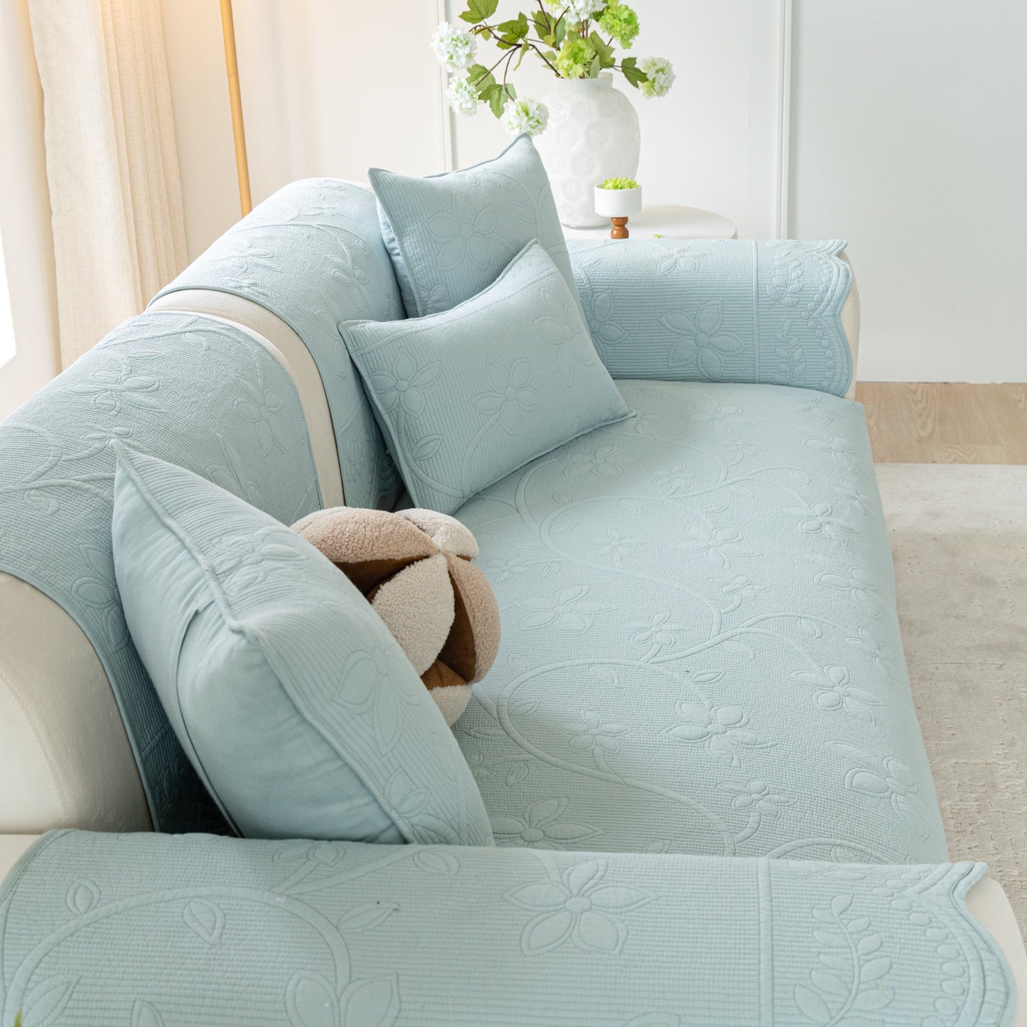 Floral Cotton Quilted Sofa Cover, Non-Slip Couch Protector with Scalloped Edges in blue on a sofa with decorative pillows.