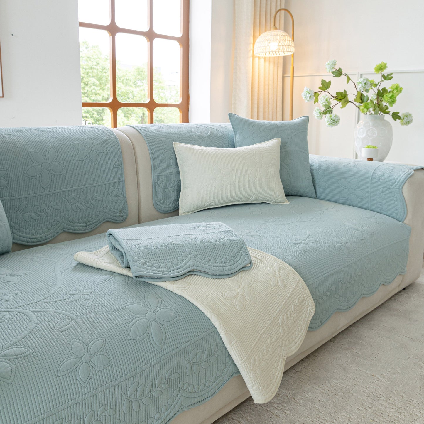 Floral Cotton Quilted Sofa Cover, Non-Slip Couch Protector with Scalloped Edges on a light blue sofa in a bright living room