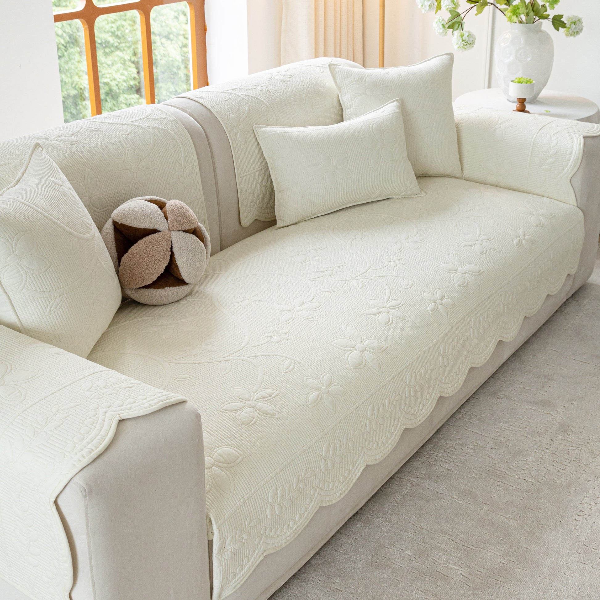 Floral Cotton Quilted Sofa Cover, Non-Slip Couch Protector with Scalloped Edges; elegant white cover on sofa with floral embroidery.