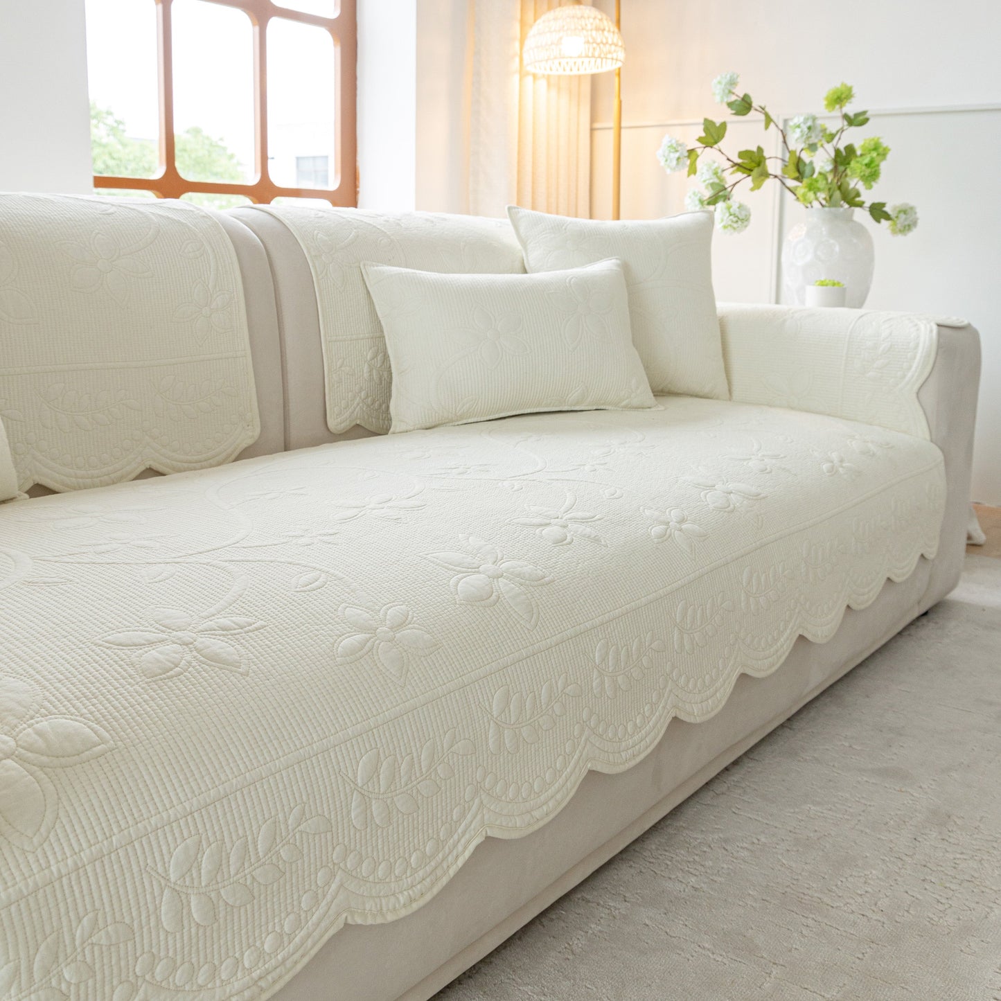 Floral Cotton Quilted Sofa Cover, Non-Slip Couch Protector with Scalloped Edges on a white sofa in a bright living room.