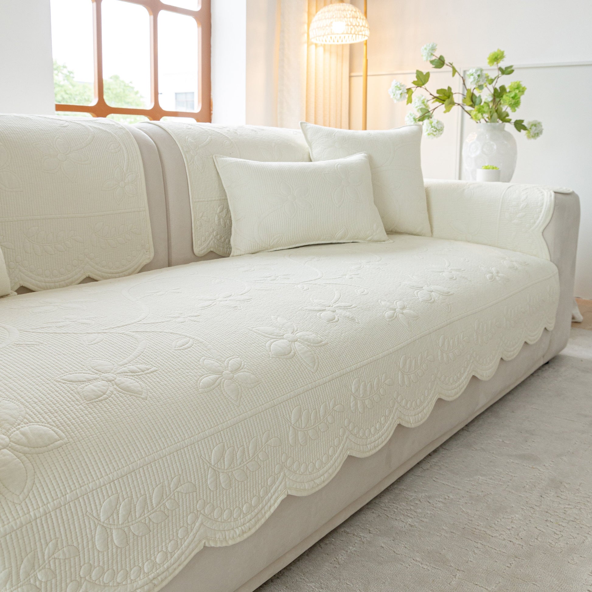 Floral Cotton Quilted Sofa Cover, Non-Slip Couch Protector with Scalloped Edges on a white sofa in a bright living room.