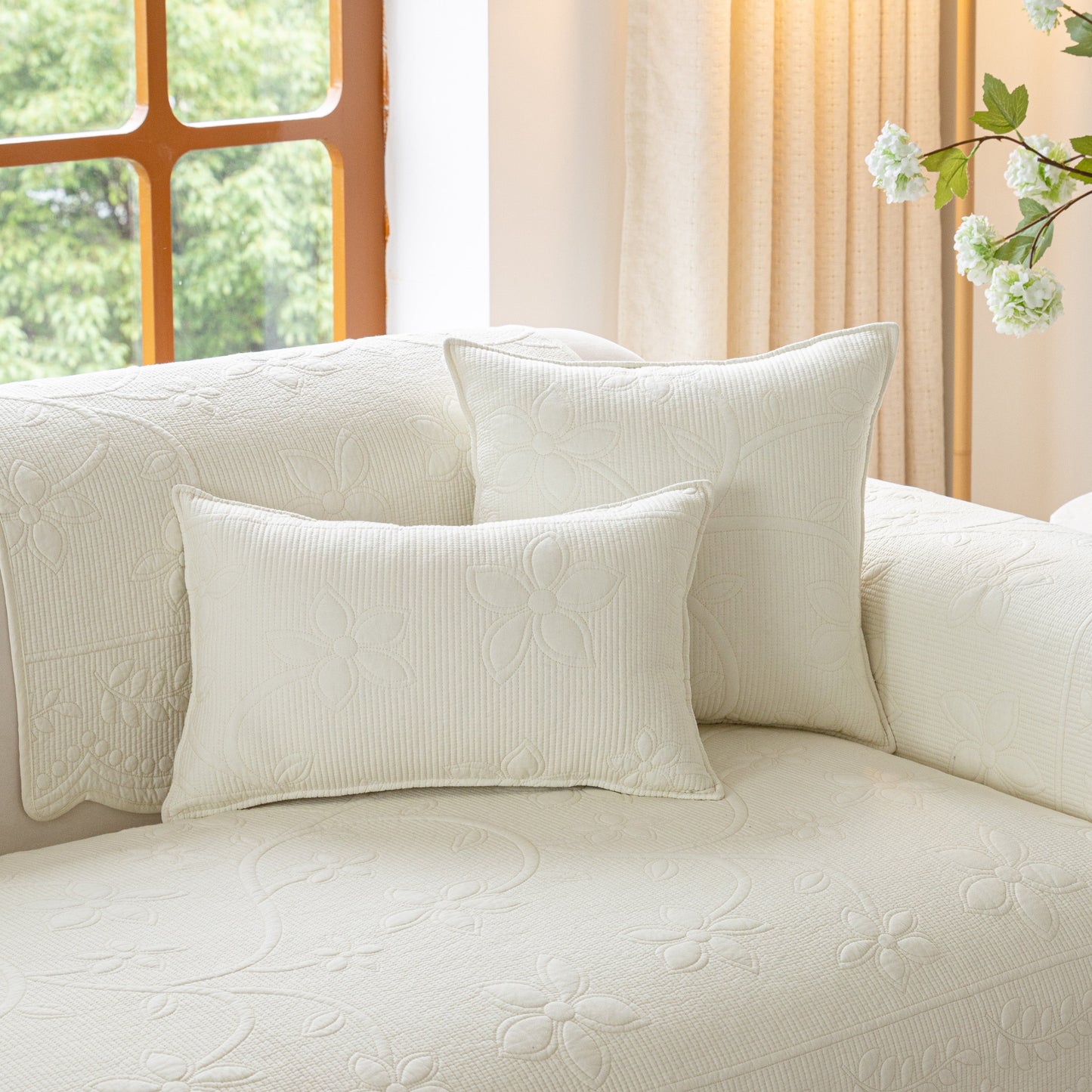 Floral Cotton Quilted Sofa Cover, Non-Slip Couch Protector with Scalloped Edges shown on a sofa with decorative pillows