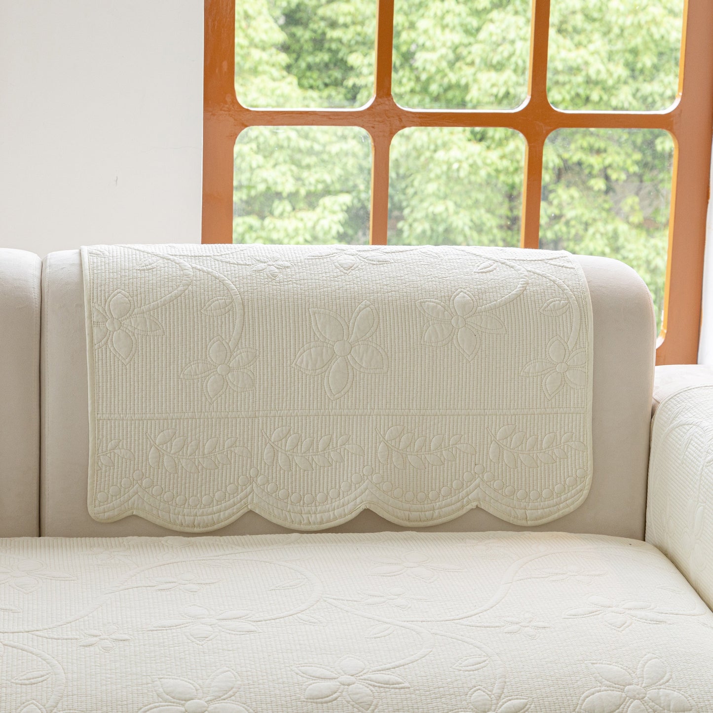 Floral Cotton Quilted Sofa Cover, Non-Slip Couch Protector with Scalloped Edges on beige couch in bright room.