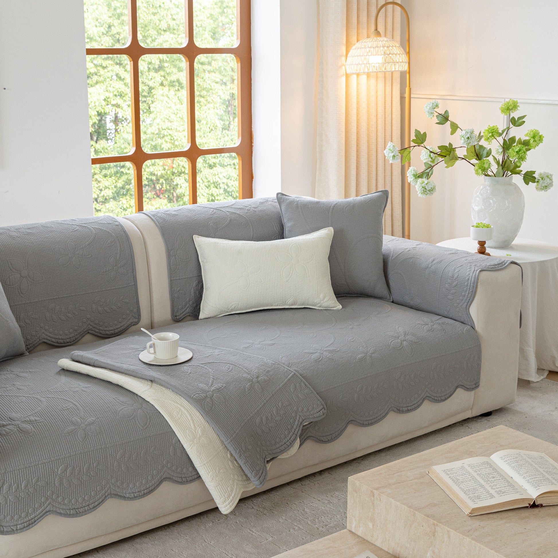 Living room with Floral Cotton Quilted Sofa Cover, Non-Slip Couch Protector with Scalloped Edges in grey, featuring cozy decor.