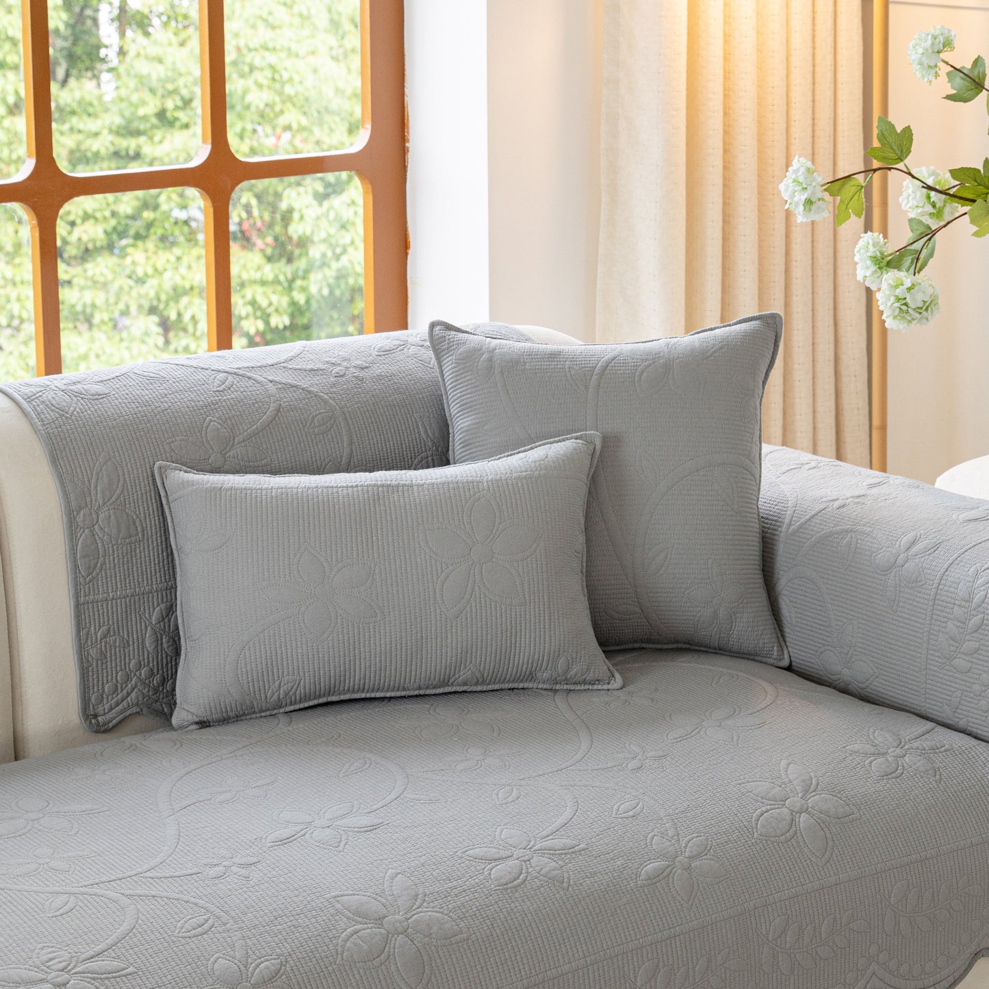 Elegant grey couch with floral quilted cover and matching pillows.