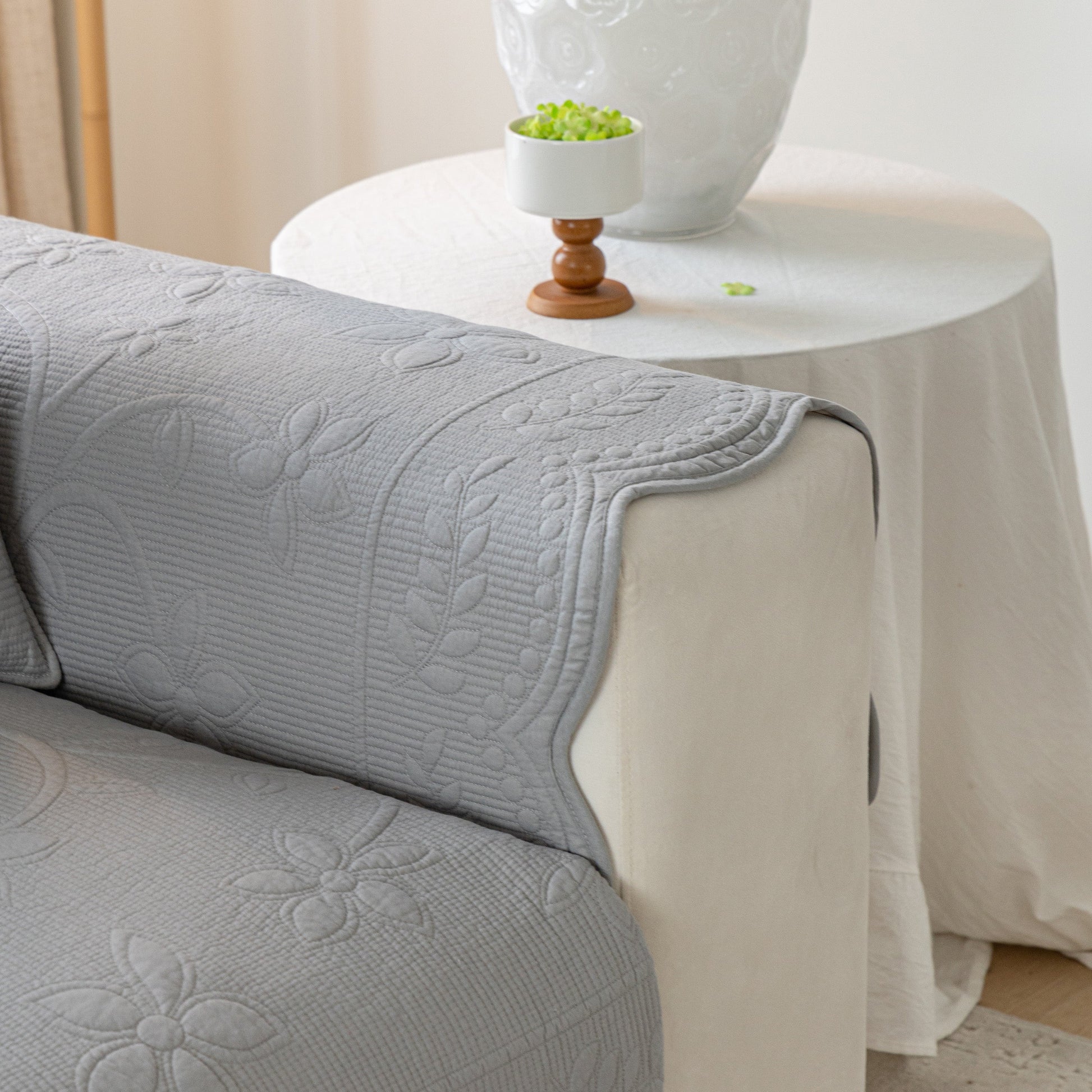 Floral Cotton Quilted Sofa Cover, Non-Slip Couch Protector with Scalloped Edges on a beige sofa.