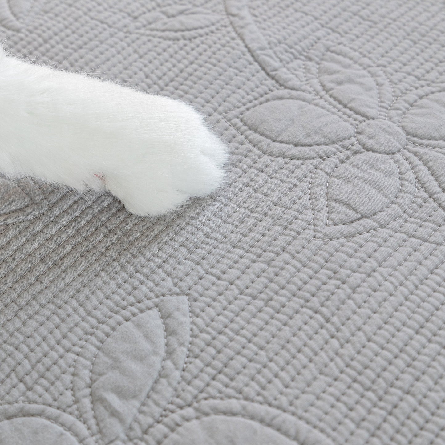 Cat paw resting on Floral Cotton Quilted Sofa Cover, Non-Slip Couch Protector with Scalloped Edges.
