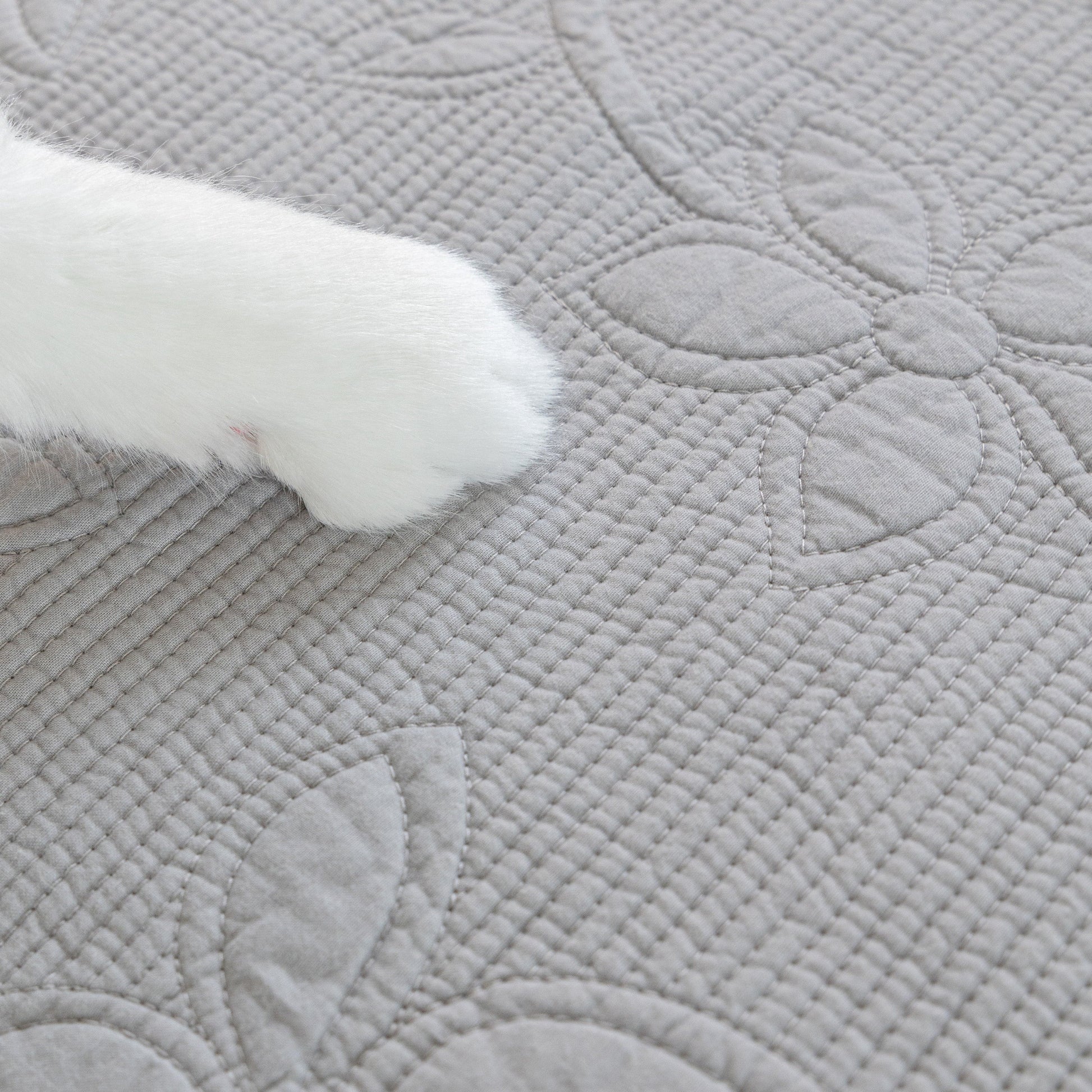 Cat paw resting on Floral Cotton Quilted Sofa Cover, Non-Slip Couch Protector with Scalloped Edges.