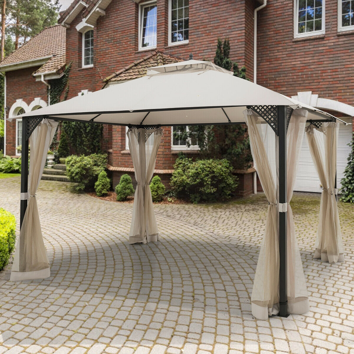12’ x 10’Outdoor Double Top Patio Gazebo-Beige in front of a brick house with open curtains and a dual-tiered roof for airflow