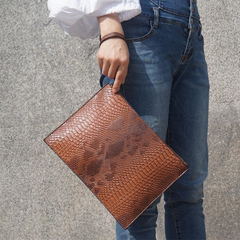 Python Luxe Clutch - Stylish Simulated Leather Clutch for Sophisticated Women held by a person wearing jeans and a white shirt.