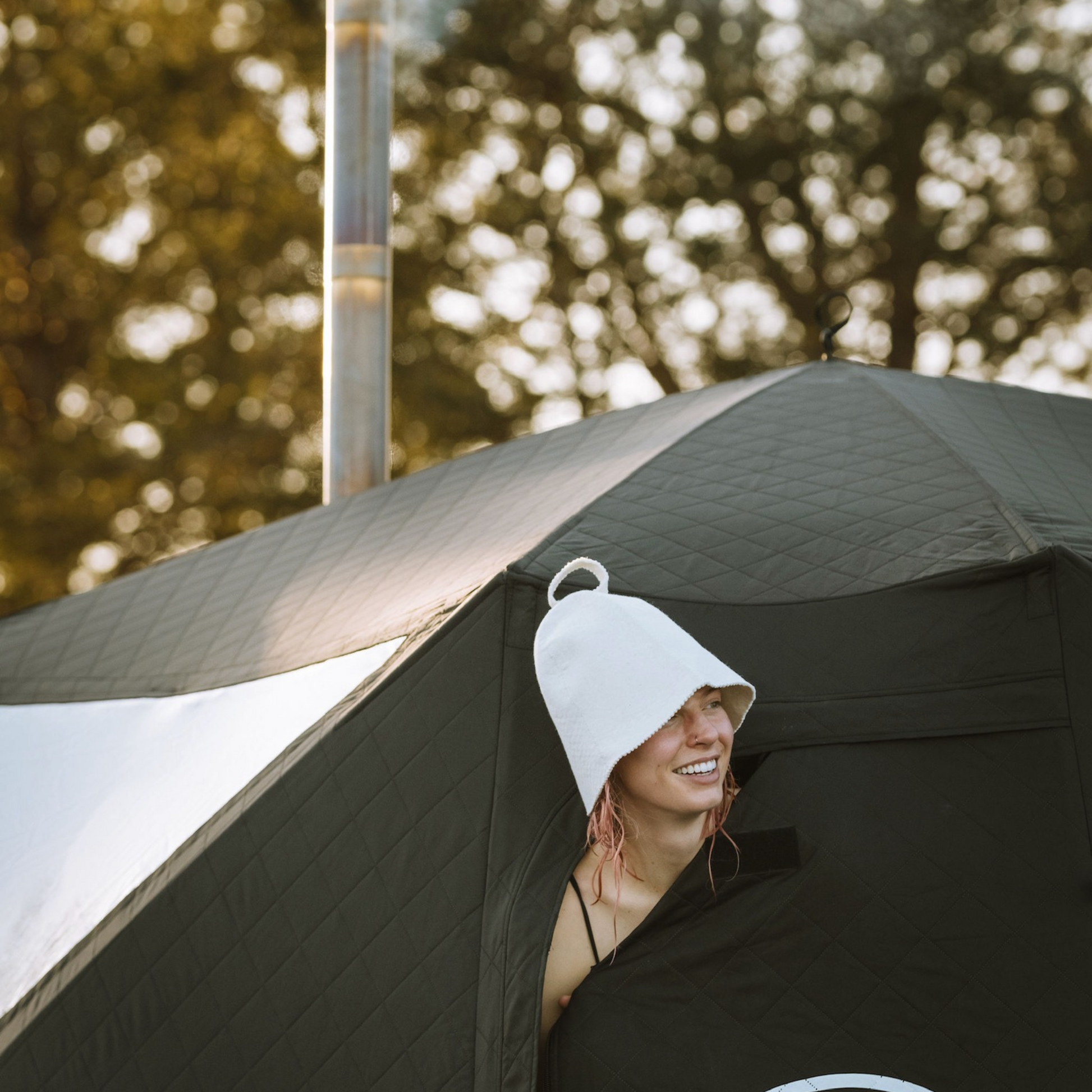 Person wearing Wool Felt Sauna Hat outside a sauna tent, smiling