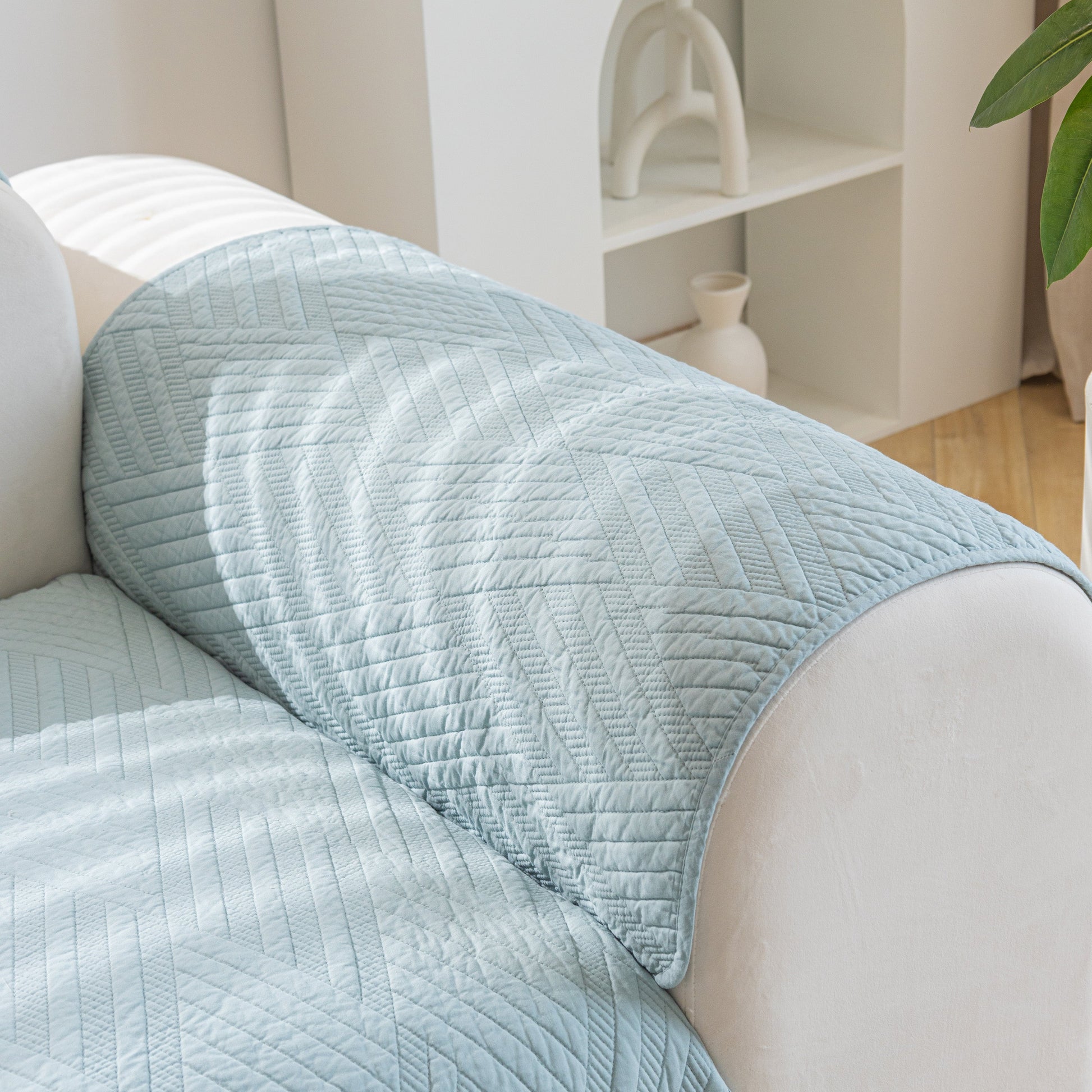 Light blue Quilted Geometric Cotton Sofa Cover, Non-Slip & Thick Padded Furniture Covers on a white sofa armrest.