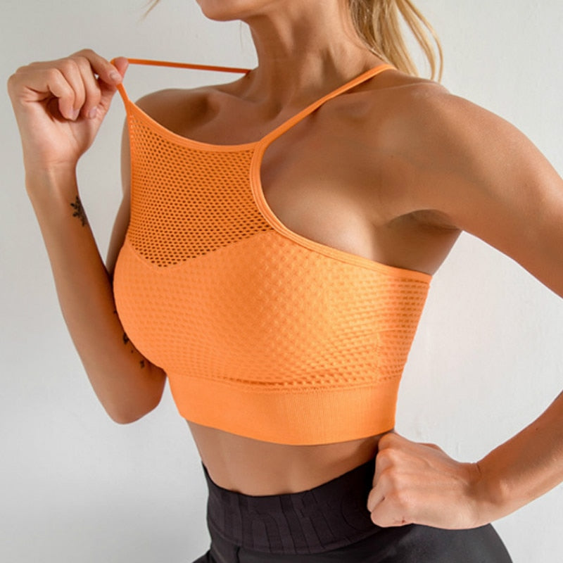 Woman wearing the Freedom Cross Back Sport Bra in orange, showcasing its breathable mesh design.