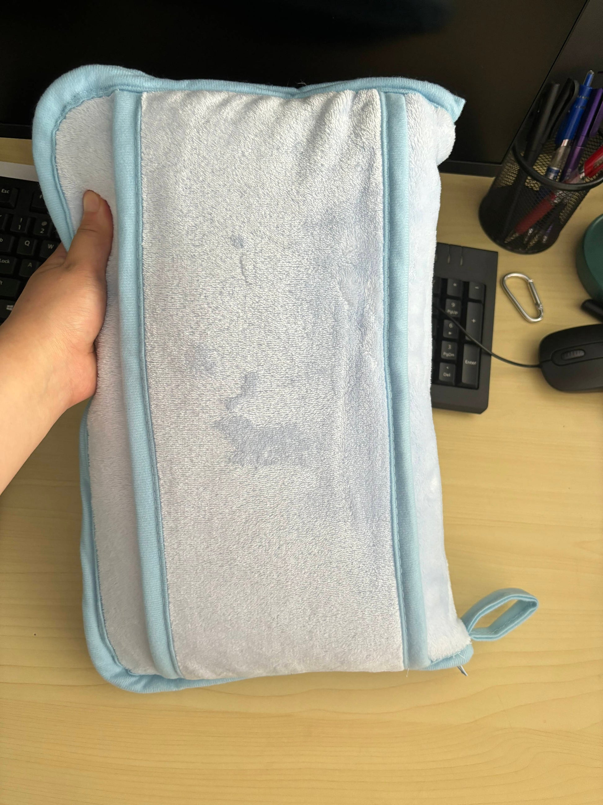 Person holding a folded Golf / Travel Blanket with carry case on desk, showcasing compact design for easy travel.