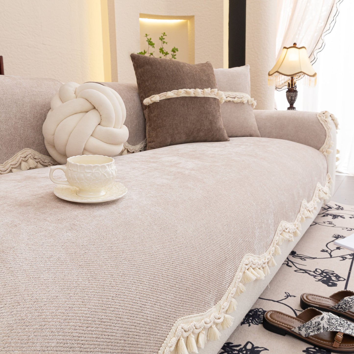 Chenille Sofa Cover Towel – Non-Slip, Washable Pets Couch Protector with Tassels on beige couch, decorative pillows, and tea cup.