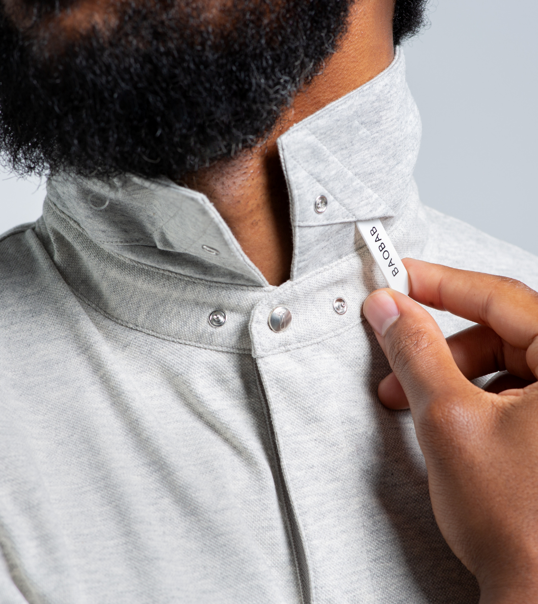 Close-up of a man adjusting the StaySharp™ Collar with hidden snaps on a Baobab Short Sleeve Perfect Polo.
