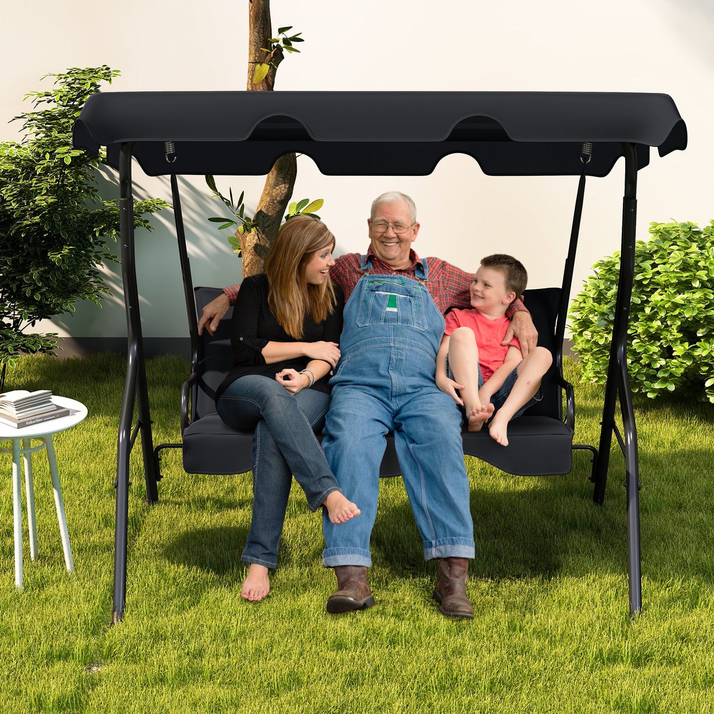 Family enjoying 3 Seat Outdoor Patio Canopy Swing with Cushioned Steel Frame-Black on a sunny day