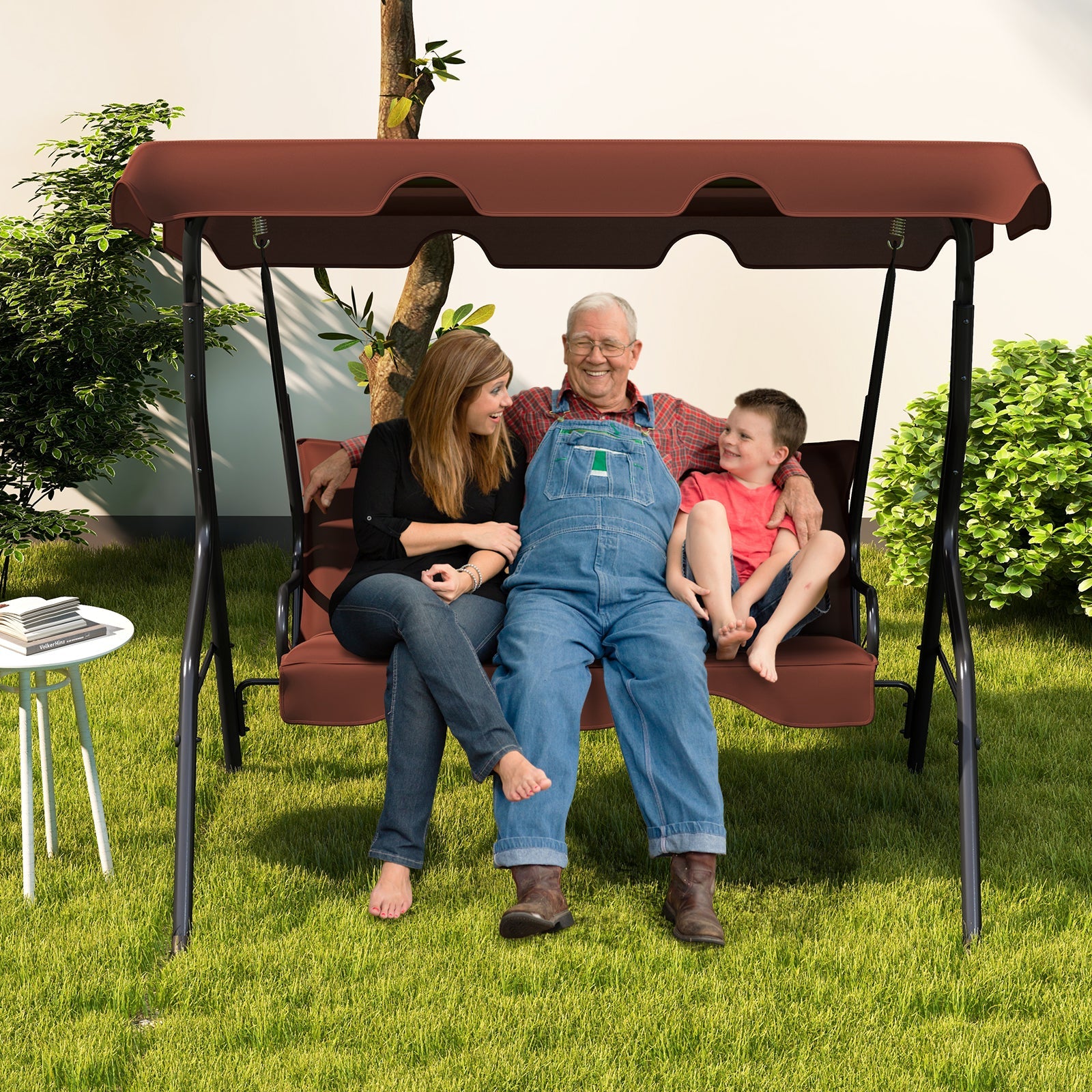 Family sitting on a 3 Seat Outdoor Patio Canopy Swing with Cushioned Steel Frame-Brown in a garden setting.