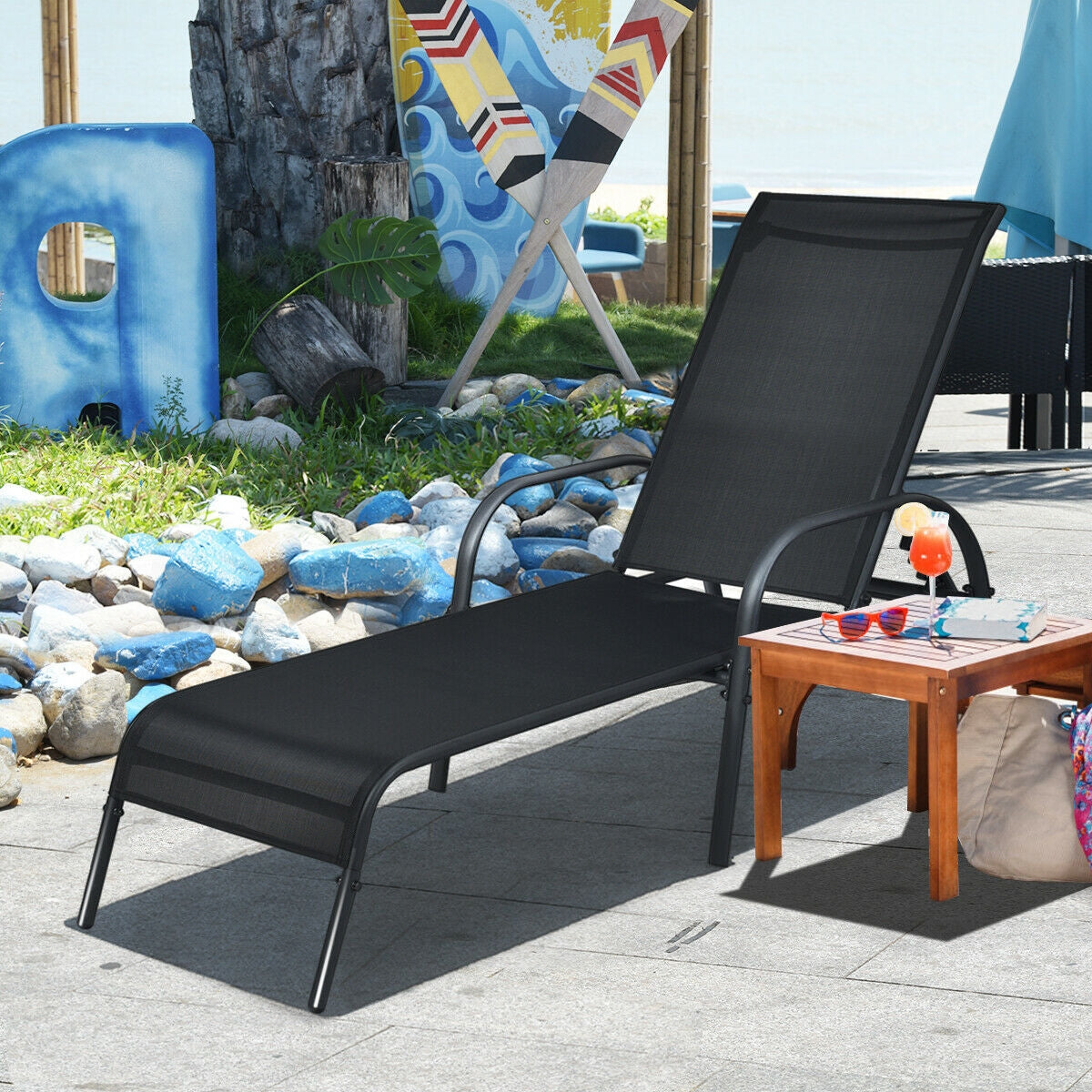 Adjustable Patio Chaise Folding Lounge Chair with Backrest-Black beside a wooden table on a sunny patio setting.