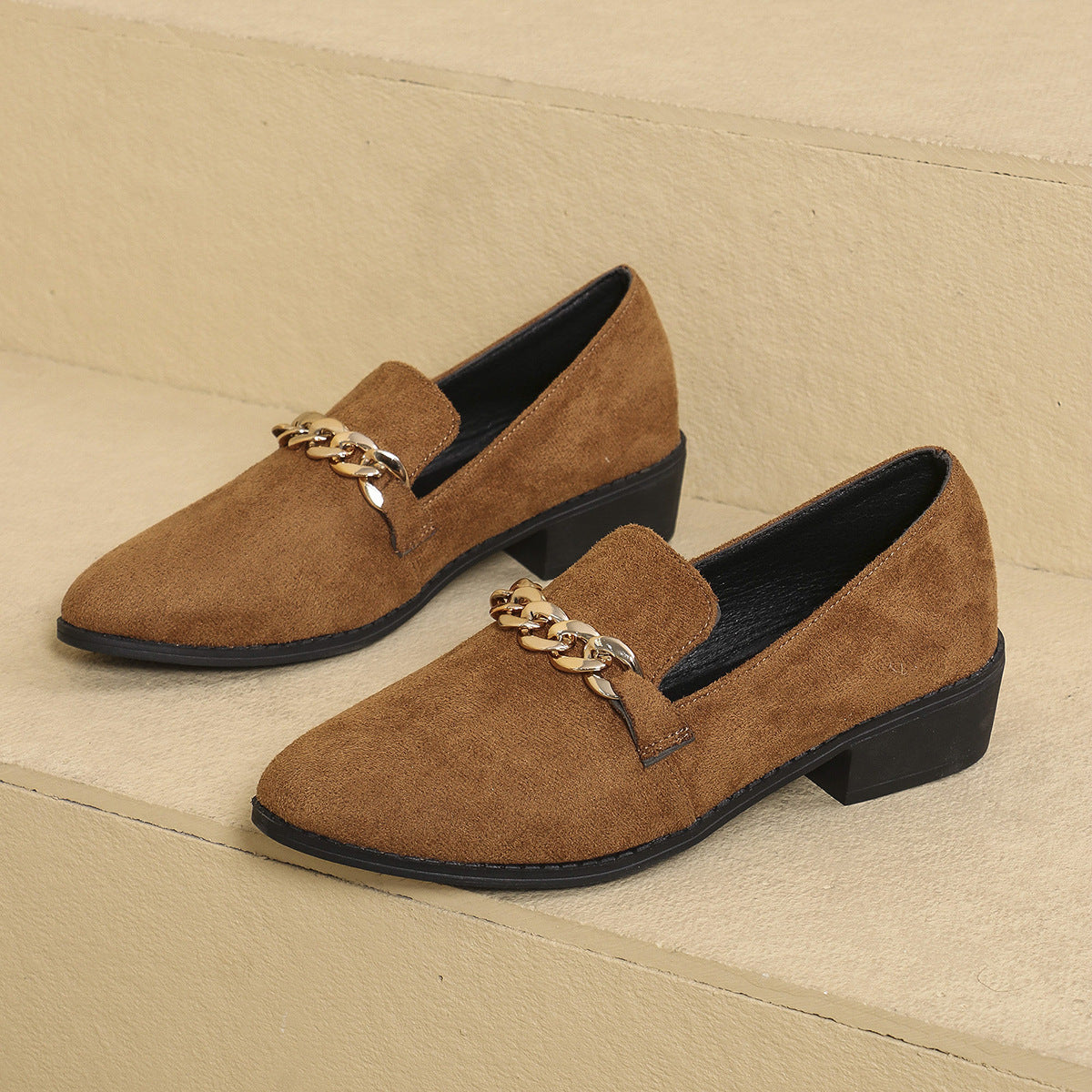 Brown suede loafers with gold chain detail on a beige background
