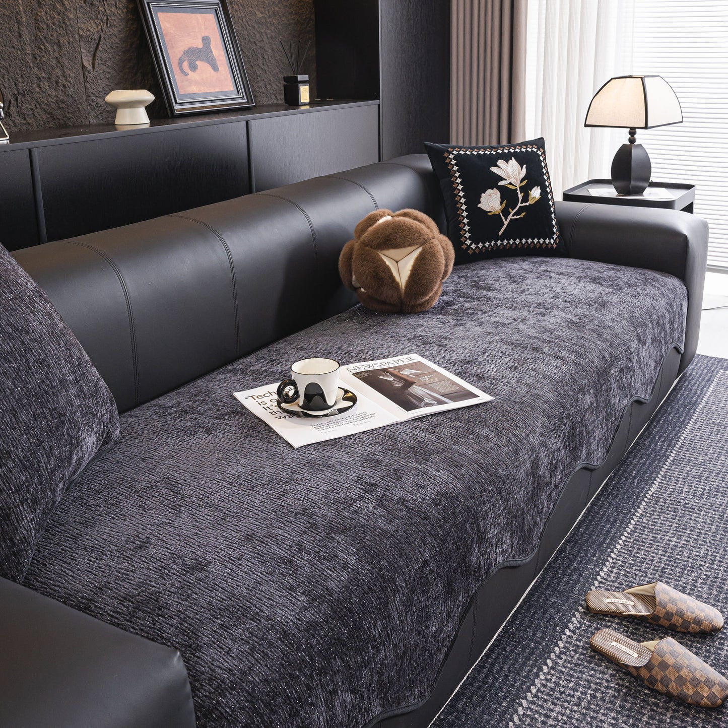 Gray Chenille Couch Cover with Scalloped Edge, Non-Slip Modular Slipcover Sectional on a black leather sofa in a modern living room.